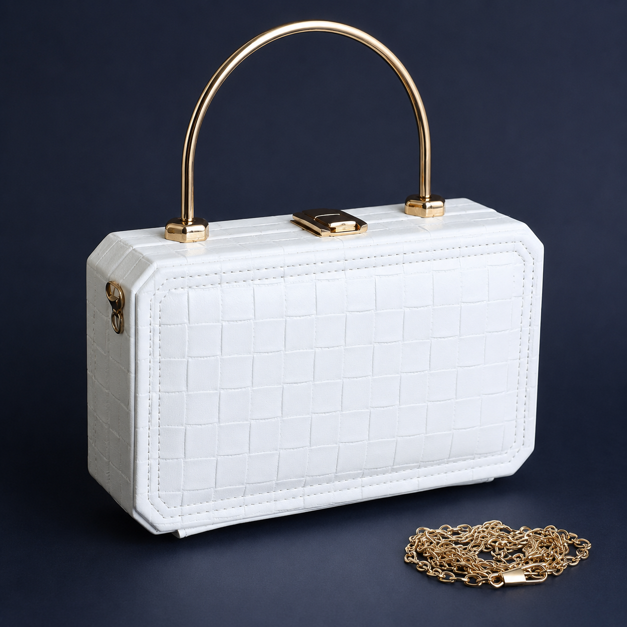 A white crocodile-embossed leather handbag with a gold arched top handle and gold clasp, shown on a dark navy background with a gold chain accessory placed in front.