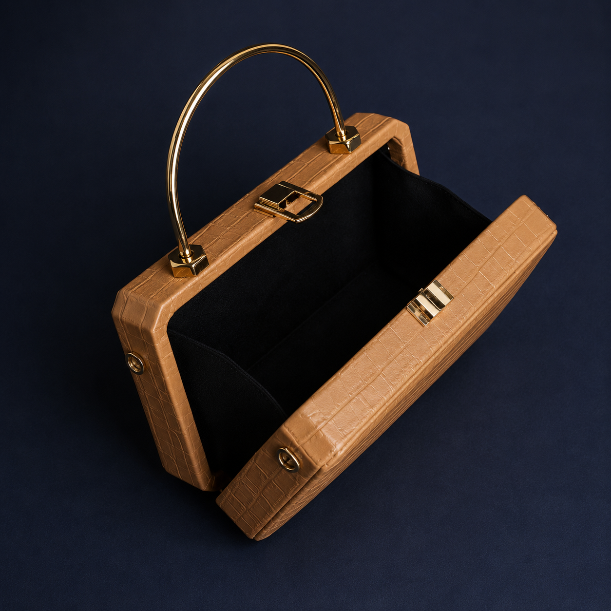 A structured handbag with a tan crocodile-embossed exterior, a gold-tone metal handle, and a black velvet interior, shown open on a dark navy background.