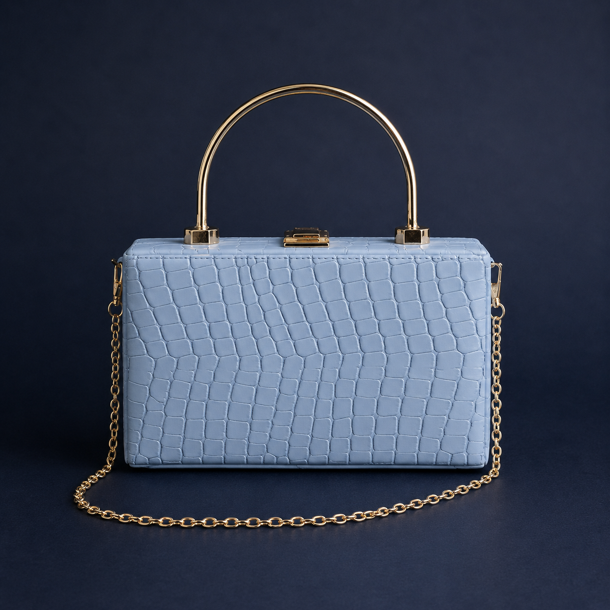 A structured light blue crocodile-embossed handbag with a gold-tone arched top handle and a matching gold chain strap, set against a dark navy background.